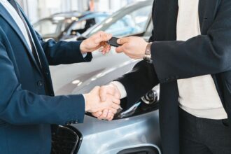 Car loan – car keys handed over with a handshake at a dealership
