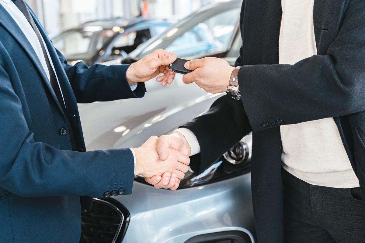 Car loan – car keys handed over with a handshake at a dealership