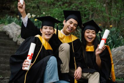 Pay off student loans – three graduates celebrating outdoors in caps and gowns holding diplomas