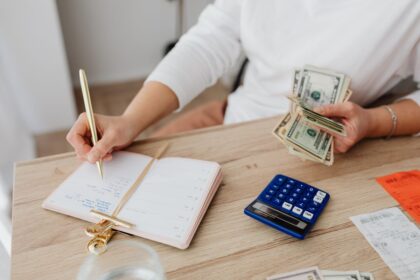 Personal finance for beginners – adult holding cash and writing in a planner while using a calculator at home