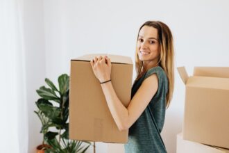 Renting your first apartment – smiling woman carrying a box into her first apartment
