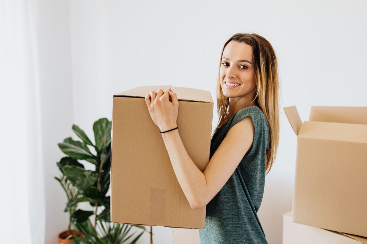 Renting your first apartment – smiling woman carrying a box into her first apartment