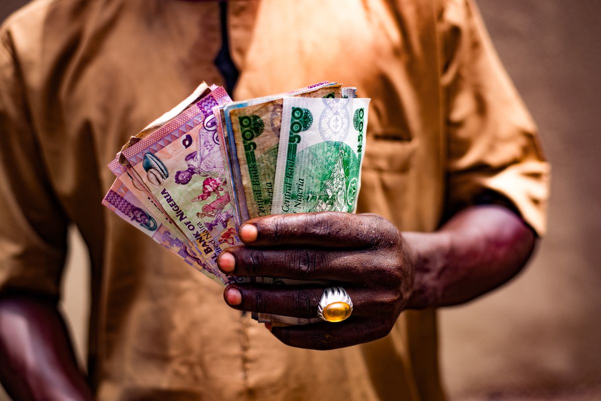 Save money in Nigeria – man holding Nigerian naira notes outdoors in Bida, Nigeria