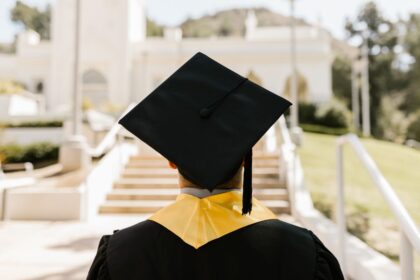 Scholarships – graduate in a cap and gown facing a university building
