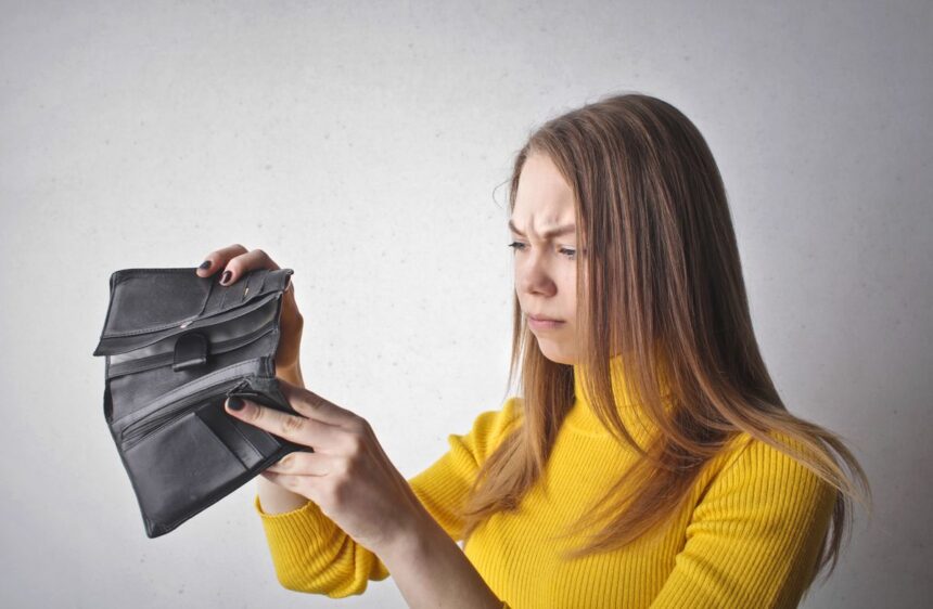 Stop living paycheck to paycheck – young woman looking at her empty wallet with a frustrated expression